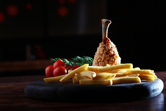 Breaded chicken leg. Breaded chicken with French fries on wooden platter. Copy space. Dark background. Beer snack