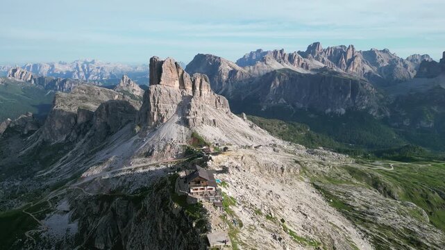 Aerial drone footage of Rifugio Nuvolau, Italy: historic mountain hut surrounded by breathtaking Dolomite scenery and dramatic rocky landscapes under clear skies. Ideal for travel and nature projects.