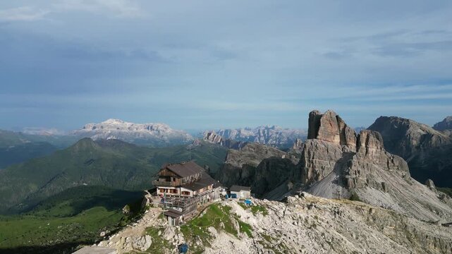 Aerial drone footage of Rifugio Nuvolau, Italy: historic mountain hut surrounded by breathtaking Dolomite scenery and dramatic rocky landscapes under clear skies. Ideal for travel and nature projects.