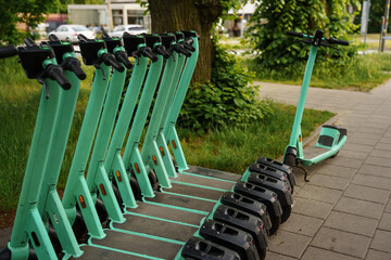 Row of green electric kick scooters parked on a city sidewalk for rental service. Urban mobility, eco friendly sharing programs, smart city transportation infrastructure, electric vehicles © Olga Yashnikova
