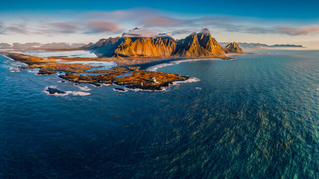 Aerial view of the dramatic Vestrahorn mountain range rising above the rugged coastline and dark volcanic sands near Vik, Myrdalshreppur, Iceland.