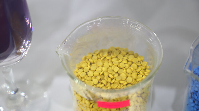Yellow plastic polymer pellets stored in a transparent laboratory beaker