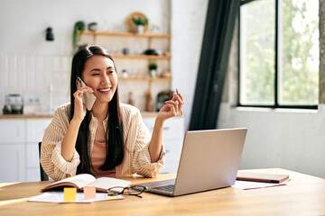Fototapeta premium Young woman on phone working at laptop in home office.