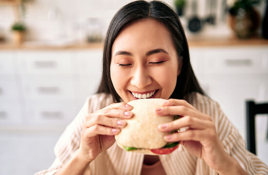 Happy young woman eating a fresh sandwich at home.