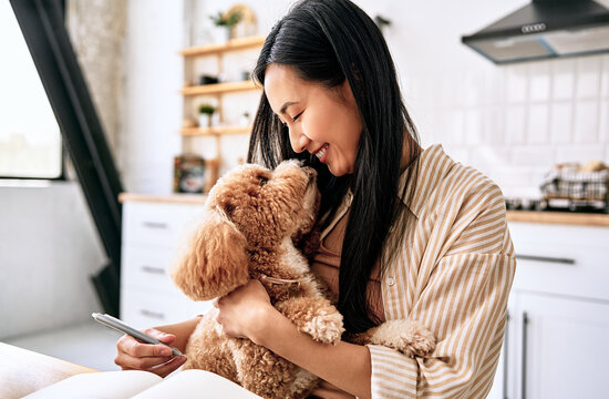 Woman cuddling a small dog in a bright kitchen.