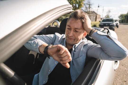 Nervous businessman checking his watch while stuck in traffic, running late for work. Urban commute stress and time pressure concept.