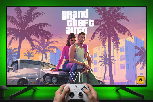Grand Theft Auto VI Key Art Displayed on TV Screen with Xbox Controller Held in Hands Against Green Backlit Setup