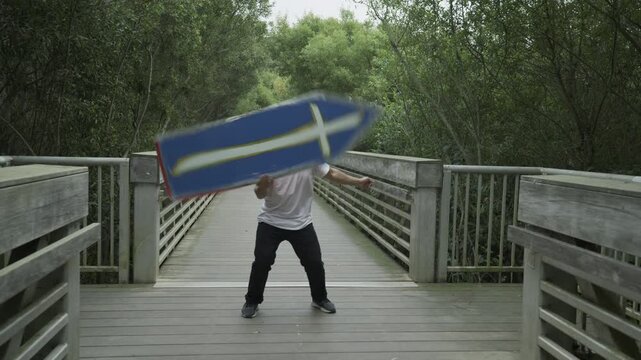 Man Spinning Blue Cross Board on Wooden Footbridge - Wide, Slow Motion