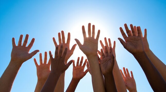 People raising hands towards the sun in a blue sky.