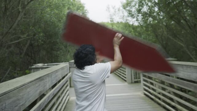 Man Ducking Under Spinning Painted Board on Wooden Footbridge