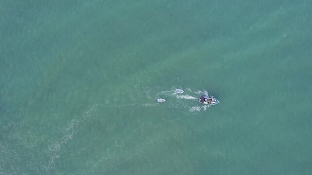 Aerial view of a motorboat towing two small dinghies across the calm turquoise waters of the Pacific Ocean near the coast of Lima, Callao Region, Peru.