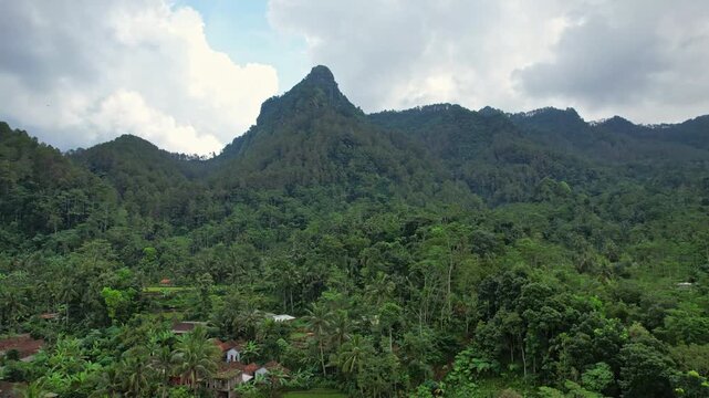 Aerial drone footage of Kepala Batu mountain, in Bruno area, Purworejo regency, Java island area, Indonesia, with forest around, some green rice fields and local houses