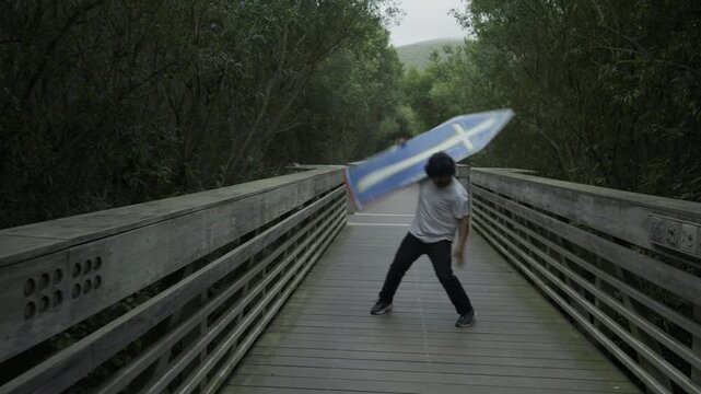 Man Spinning Painted Board on Wooden Footbridge - Wide Angle