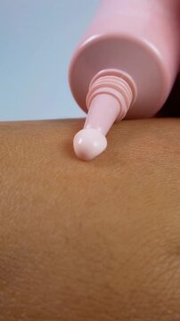 Pouring a small amount of pink moisturizing cream onto skin from bottle packaging. Beauty concept, soft pink texture for daily skincare hydration.