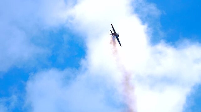 A sports plane performing aerobatics with a smoke trail.
