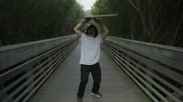 Man Spinning Painted Board Overhead on Wooden Footbridge - Steady Cam Shot