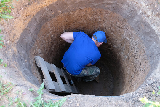 Worker digs a cesspool manually with a shovel at a construction site. Manual excavation work.