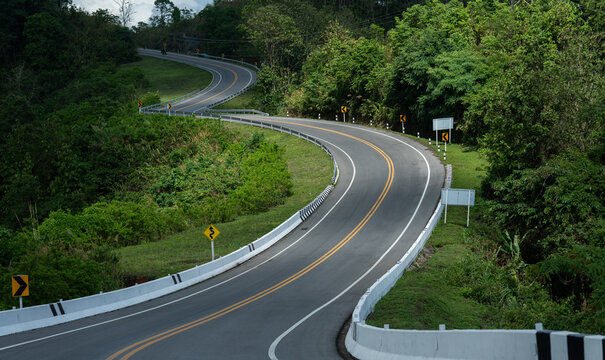 Winding road through lush green forest with clear sky, showcasing nature beauty and tranquility