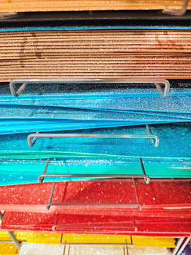 Stacks of colorful felt fabric sheets, paper in orange, red, green, brown, and blue on a metal shelf. Craft materials displayed in a store, ideal for art and DIY projects.
