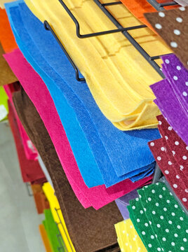 Stacks of colorful felt fabric sheets, paper in orange, red, green, brown, and blue on a metal shelf. Craft materials displayed in a store, ideal for art and DIY projects.
