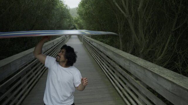 Joyful Man Spinning Painted Board Above Head on Footbridge - Medium Close-Up