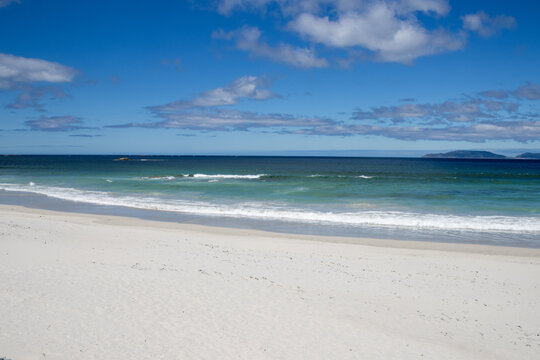 Praia de Carnota in A Coru&ntilde;a, Galicia, Spain. The image showcases the expansive white sand shoreline, gentle turquoise ocean waves breaking on the coast, and the dramatic silhouette of Monte Louro 