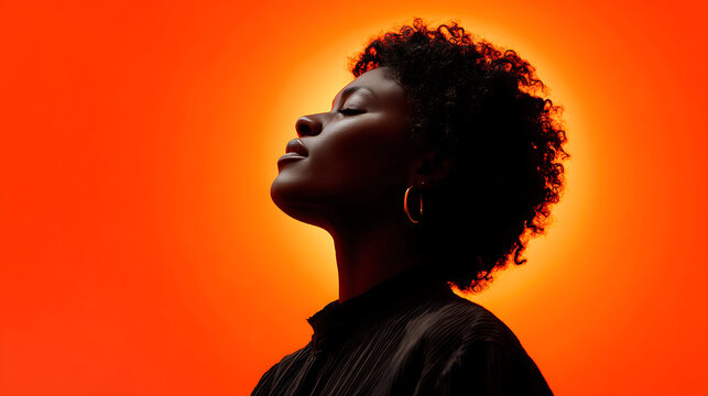 silhouette of african american woman with afro hair profile view against vibrant orange background 