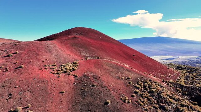 Aerial view of the Mauna Kea cinder cone and Mauna Loa volcano landscape featuring red volcanic soil and dark lava fields in Hawaii County, Hawaii, United States.