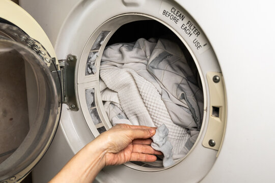 Hand removing lint debris from clothes dryer after drying white blankets. The debris is trapped in the dryer's filter.
