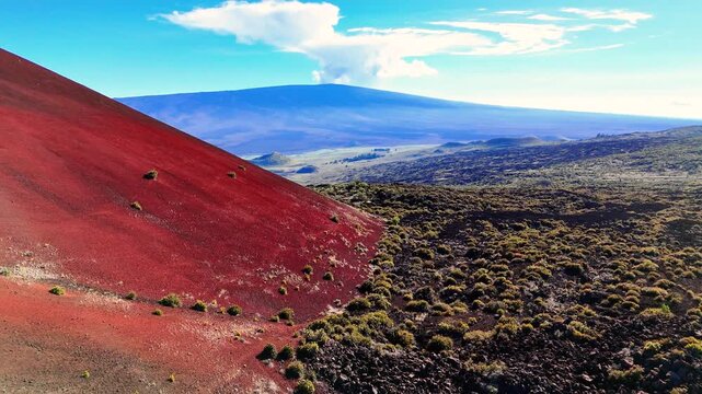 Aerial view of the Mauna Kea cinder cone and Mauna Loa volcano landscape featuring red volcanic soil and dark lava fields in Hawaii County, Hawaii, United States.