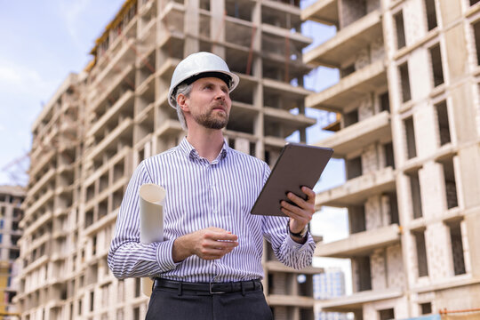 Engineer man in helmet use tablet computer for controls construction of skyscrapers, background buildings under construction.