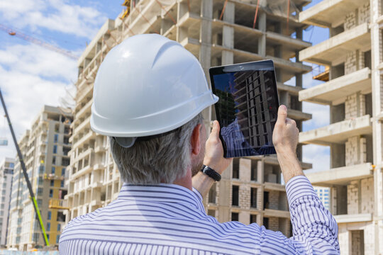 Construction engineer in helmet with the tablet pictures of objects on a construction site