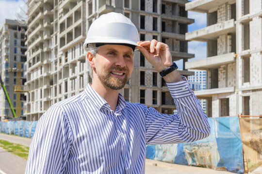 Young smiling man architect wearing a helmet looking to building under construction