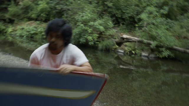 Man Swinging And Spinning Painted Board Beside Forest Stream - Tilt, Steady Cam Shot