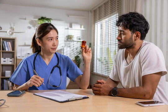 Doctor patient capsule consultation clinic medicine Asian female physician showing red pill bottle to male patient during medical appointment in bright office
