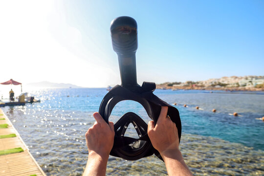 Woman holding a snorkeling mask up against the bright blue sky with the sea in the background.