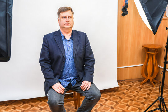 A man sits on a chair in a photo studio, preparing for a photo shoot for documents and a passport.