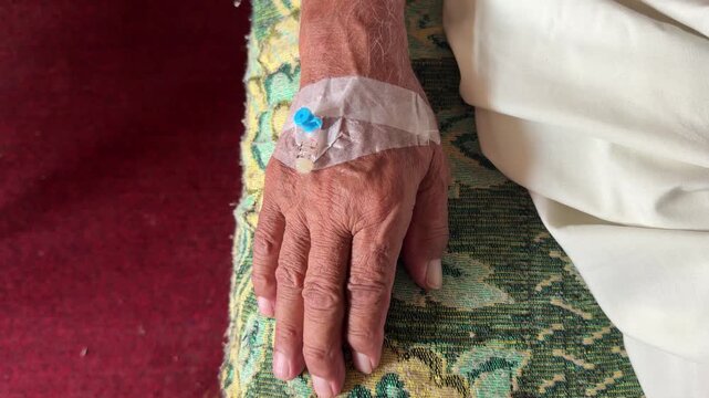 A comforting hand gently holds elderly hand with IV cannula secured by clear medical tape.