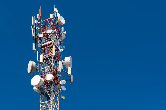 Telecommunication mast equipped with advanced 5G cellular antennas and microwave sector dishes for high-speed wireless network transmission, isolated on clear blue sky backdrop,   with copy space