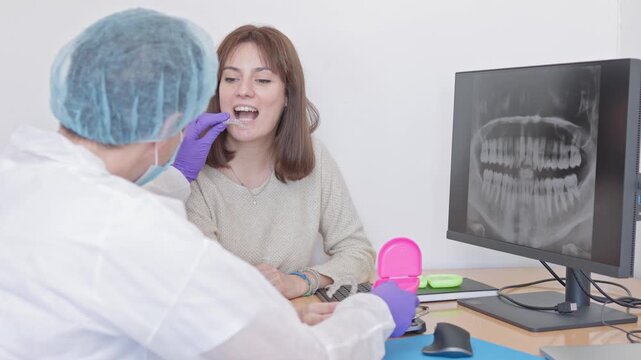 Professional orthodontist showing a female patient how to use invisible aligners, explaining the treatment by pointing at a jaw x-ray on the computer screen in the dental clinic