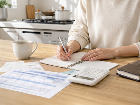 Woman calculating household budget and writing notes at kitchen counter