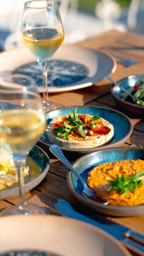 Outdoor Lunch Spread: A delightful outdoor dining experience featuring small plates of gourmet appetizers and glasses of crisp white wine, set on a rustic wooden table under the warm sun.