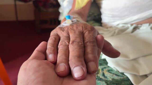 A comforting hand gently holds elderly hand with IV cannula secured by clear medical tape.