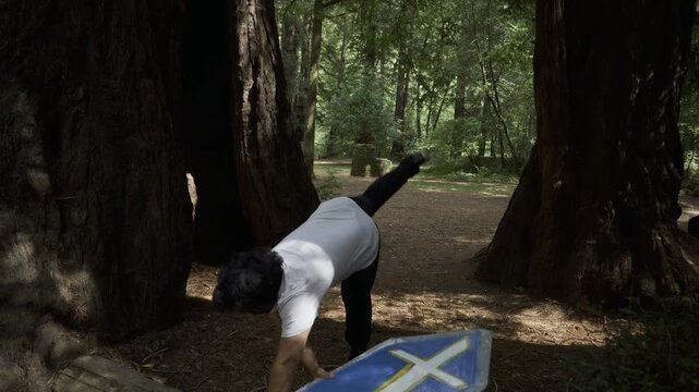 Man Swinging Blue Painted Board Among Giant Redwood Trunks And Doing Backflip - Steady Cam Shot