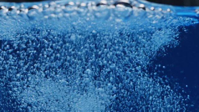 Clear bubbles rise through deep blue liquid in a container