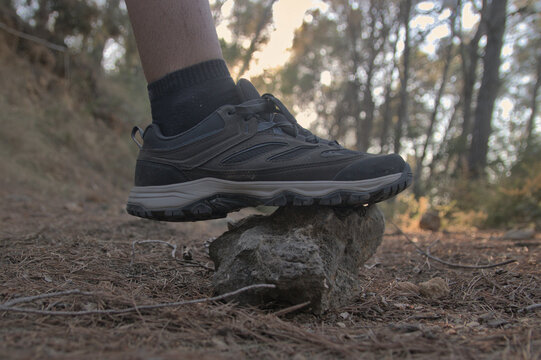 Detalle de zapatillas de senderismo pisando suelo con piedras y pinocha en un bosque