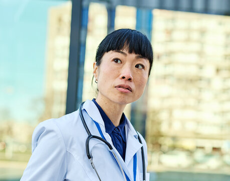 Portrait of an asian female woman doctor or nurse and  health care worker holding a cup of coffee and using a tablet computer in front of hospital or clinic outside