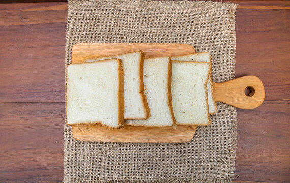 Fresh sliced ​​bread arranged on a wooden cutting board with one slice leaning against the stack over a rustic wooden table. top view copy space.