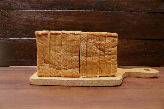 Fresh sliced bread arranged on a wooden cutting board over a rustic wooden table. Fresh delicious gourmet food background on the table rustic side view copy space.
