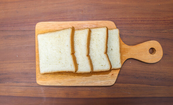 Fresh sliced ​​bread arranged on a wooden cutting board with one slice leaning against the stack over a rustic wooden table. top view copy space.